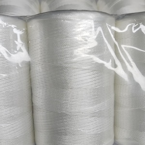 May include: Close-up of several spools of white thread, tightly wound and packaged in clear plastic. The thread appears to be a bright white color, with a slightly textured surface. The spools are cylindrical in shape and are stacked together.