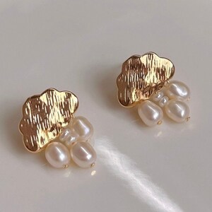 Puede incluir: Un par de pendientes de nube de oro con detalles de perlas. Cada pendiente presenta una nube de oro texturizada con un racimo de peque&ntilde;as perlas blancas que cuelgan de la parte inferior.