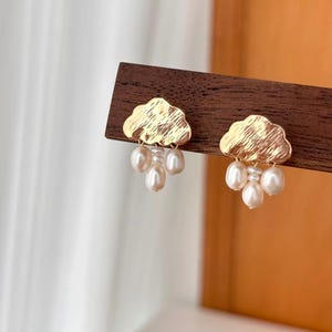 Puede incluir: Pendientes de oro en forma de nube con un racimo de perlas blancas que cuelgan de cada nube.