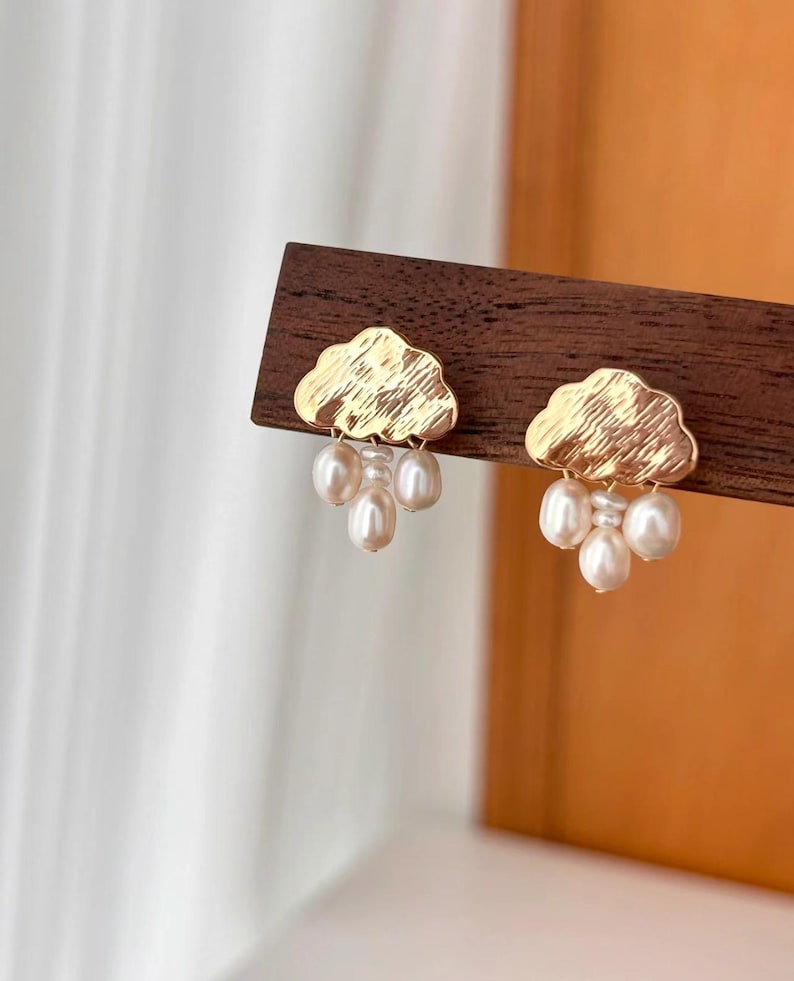 Puede incluir: Pendientes de oro en forma de nube con un racimo de perlas blancas que cuelgan de cada nube.