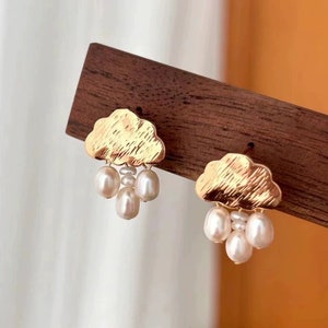 Puede incluir: Pendientes de oro en forma de nube con un racimo de perlas blancas que cuelgan de cada nube.