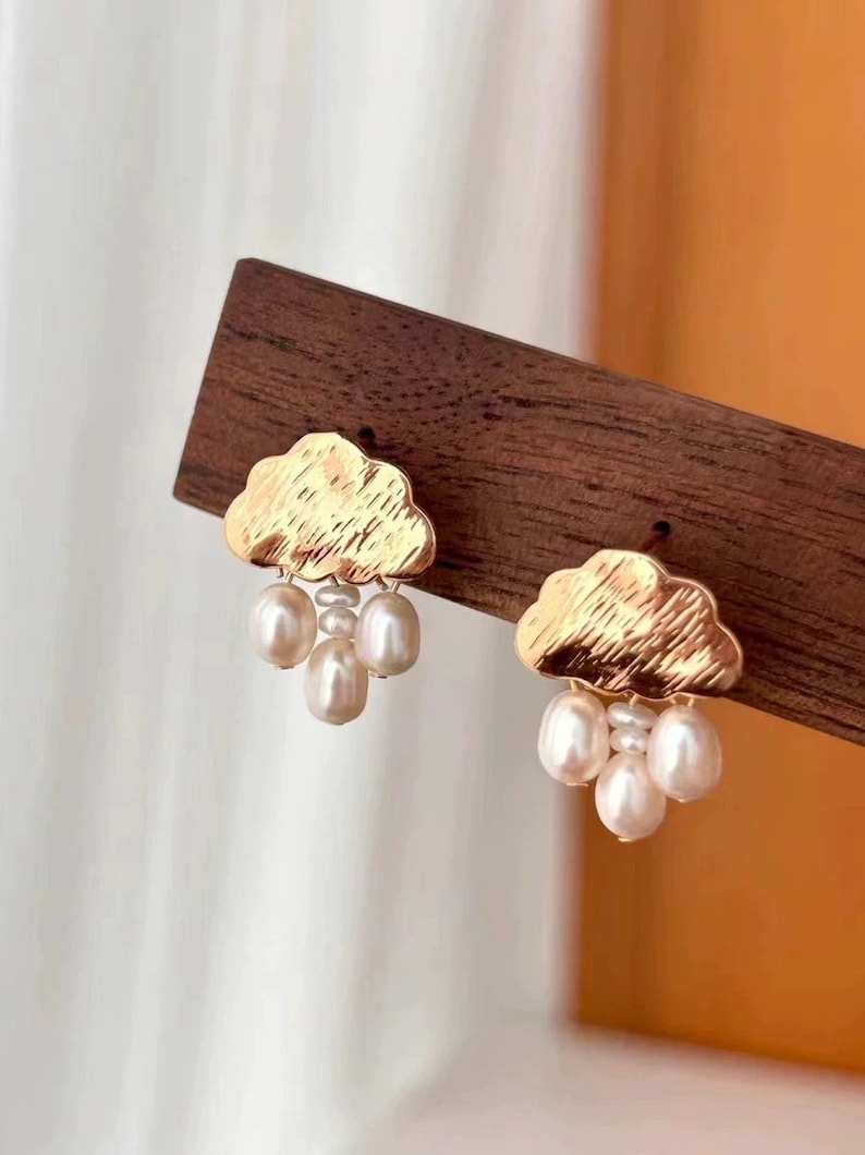 Puede incluir: Pendientes de oro en forma de nube con un racimo de perlas blancas que cuelgan de cada nube.