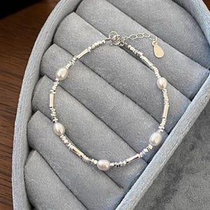 May include: A silver bracelet with small silver beads and four white pearls. The bracelet is displayed in a blue velvet jewelry box.