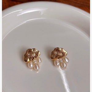 Puede incluir: Un par de pendientes de nube de oro con gotas de perlas. Los pendientes est&aacute;n sobre una superficie blanca.