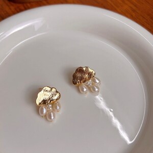 Puede incluir: Un par de pendientes de nube de oro con gotas de perlas colgantes. Los pendientes est&aacute;n en un plato blanco.
