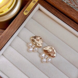 Puede incluir: Un par de pendientes de nube de oro con gotas de perlas colgantes. Los pendientes se muestran en una caja de madera con un forro de terciopelo blanco.