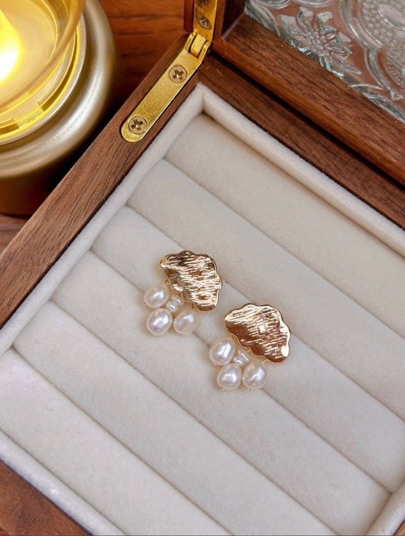 Puede incluir: Un par de pendientes de nube de oro con gotas de perlas colgantes. Los pendientes se muestran en una caja de madera con un forro de terciopelo blanco.