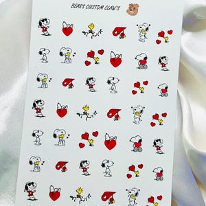 Pu&ograve; includere: Foglio di adesivi per nail art con Snoopy, Woodstock, cuori e altri personaggi dei Peanuts. Gli adesivi sono rossi, neri, bianchi e gialli. Il testo "BEARS CUSTOM CLAW'S" &egrave; stampato in alto.