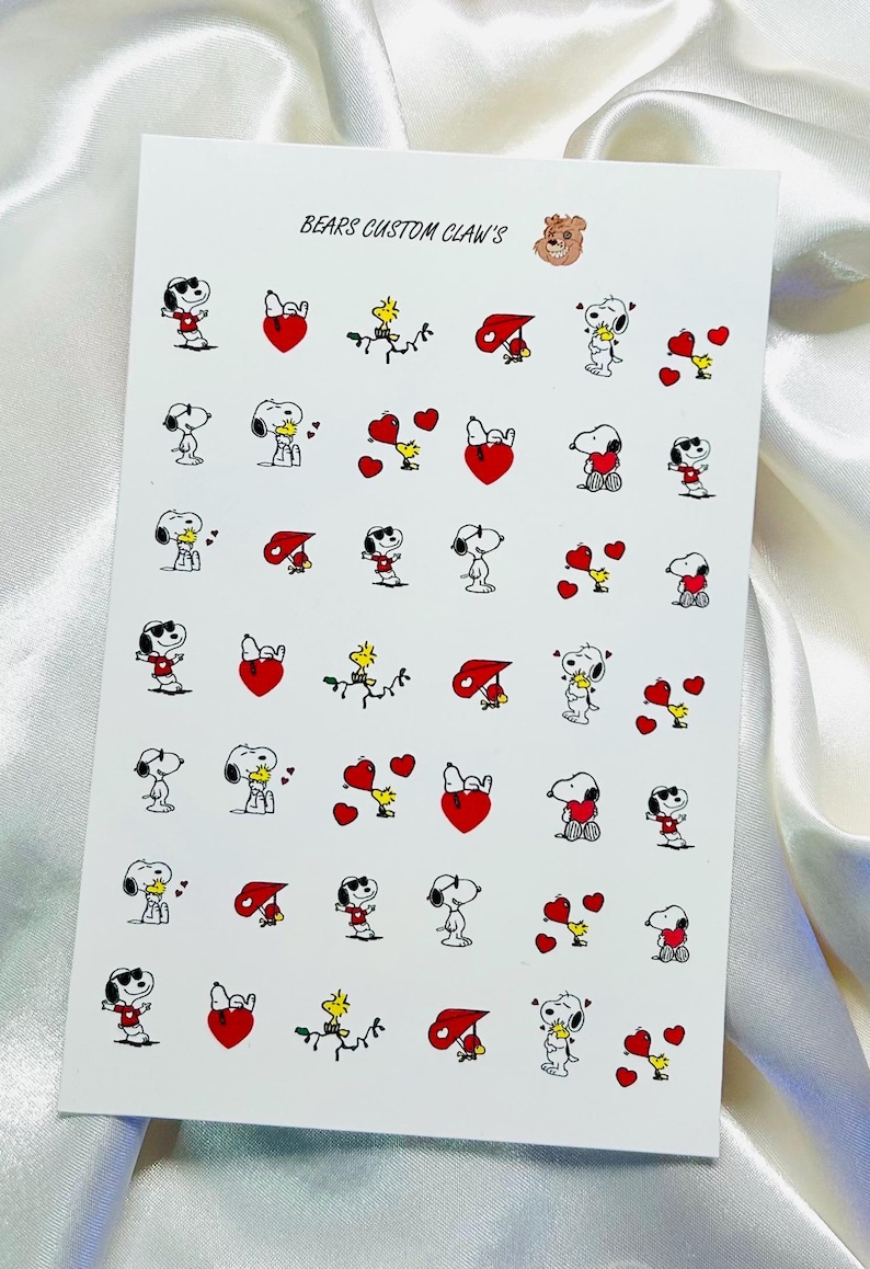 Pu&ograve; includere: Foglio di adesivi per nail art con Snoopy, Woodstock, cuori e altri personaggi dei Peanuts. Gli adesivi sono rossi, neri, bianchi e gialli. Il testo "BEARS CUSTOM CLAW'S" &egrave; stampato in alto.