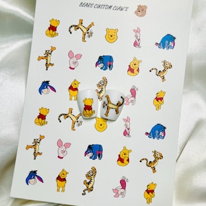 Può includere: Foglio di adesivi per nail art con personaggi di Winnie the Pooh. Include immagini di Pooh, Tigro, Pimpi ed Eeyore. Il testo "BEARS CUSTOM CLAW'S" è stampato in alto. Due tip per unghie bianche sono decorate con Pooh e Tigro.