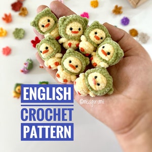 Puede incluir: Una mano sosteniendo un grupo de pequeños pollitos amarillos tejidos a crochet con gorros verdes con capucha. El texto "ENGLISH CROCHET PATTERN" está escrito en letras blancas sobre un fondo azul. El texto "@missgurumii" está escrito en letras negras sobre un fondo blanco.