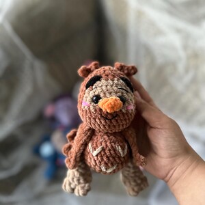 以下が含まれることがあります： 茶色、ベージュ、オレンジ色の手作りの編みぐるみフクロウ人形。 フクロウは黒い目、オレンジ色のくちばし、ピンクの頬をしています。 人形は質感のある外観をしています。