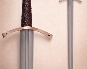 Op de afbeelding: Een stalen zwaard met een tweesnijdend lemmet, een donkerbruine, getextureerde lederen greep en een bronskleurige pareerstang met kleine kruisgravures. De pommel is achthoekig met een centraal kruisembleem. Tekst luidt HSKNIVESTRADERS.
