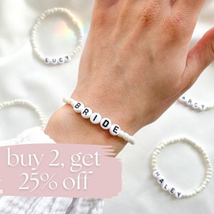 May include: White beaded bracelets with the words "BRIDE", "LUCY", "ARCY", and "HALEY" spelled out in black letters. The bracelets are on a white surface. The text "buy 2, get 25% off" is written in pink on a white background.