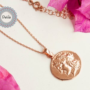 Pode incluir: Colar em ouro rosa com um pendente circular com um relevo cl&aacute;ssico. A corrente e o pendente s&atilde;o exibidos sobre um fundo neutro, com elementos florais cor-de-rosa. Uma joia delicada.