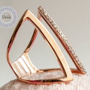 May include: A rose gold ring with a geometric design. The ring has a thin band with a row of small clear stones.
