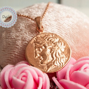 Pode incluir: Um colar em ouro rosa com um pingente redondo que apresenta um perfil detalhado. O pingente est&aacute; pendurado em uma corrente fina. A imagem inclui rosas cor-de-rosa e um fundo rosa suave.