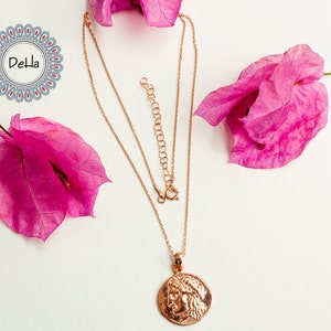 Pode incluir: Colar de ouro rosa com um pingente com um perfil cl&aacute;ssico. O colar &eacute; exibido em uma superf&iacute;cie branca, acentuado por flores de buganv&iacute;lias rosa. A corrente &eacute; ajust&aacute;vel.
