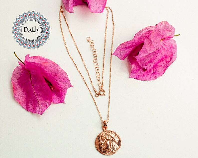 Pode incluir: Colar de ouro rosa com um pingente com um perfil cl&aacute;ssico. O colar &eacute; exibido em uma superf&iacute;cie branca, acentuado por flores de buganv&iacute;lias rosa. A corrente &eacute; ajust&aacute;vel.