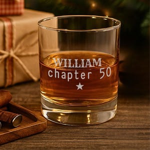 Peut inclure: Un verre transparent rempli d'un liquide ambré, gravé de "WILLIAM chapitre 50" et d'une étoile. Le verre est posé sur une surface en bois, avec un coffret cadeau et des cigares en arrière-plan. Un article de bar pour célébrer.