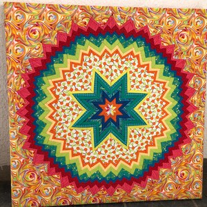 Peut inclure: Une courtepointe colorée avec un motif en étoile éclatante dans des tons de rouge, orange, jaune, vert, bleu et blanc. L'étoile éclatante est entourée d'un motif tourbillonnant d'orange, de jaune et de rouge.