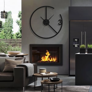 May include: A modern living room with a black fireplace, a black leather sofa, and a large black clock on the wall. The clock has a unique design with a circle and a line through it. The room is decorated in a minimalist style with a gray rug and two round coffee tables.