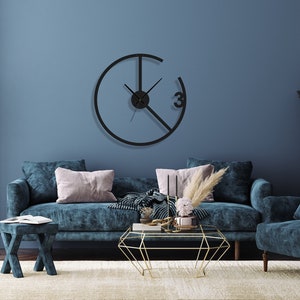May include: A living room interior with a blue velvet sofa, a matching armchair, and a gold geometric coffee table. A black clock with a unique design hangs on the wall. The room is decorated with a vase of pink flowers and a floor lamp.
