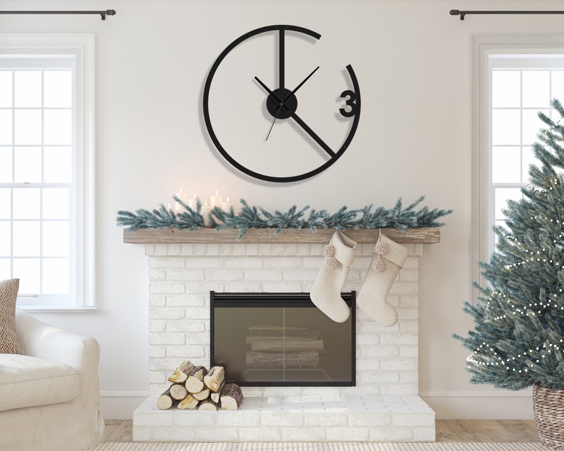 May include: A black metal clock with a circular design and Roman numeral markings. The clock is hanging on a white wall above a fireplace with a white brick surround. The fireplace has a black metal grate and a pile of logs in front of it. There are two white stockings hanging from the mantelpiece.