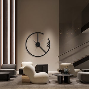 May include: A modern black wall clock with a circular design and a single Roman numeral "3" on the face. The clock is hanging on a beige wall in a living room setting with two white armchairs and a black coffee table.