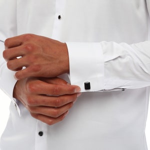 May include: A white dress shirt with black cufflinks. The shirt has a button-down collar and long sleeves.