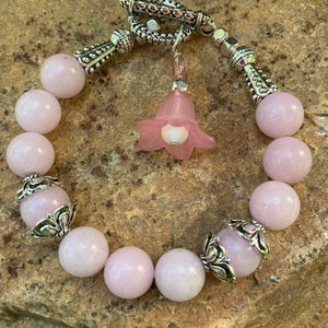 May include: A pink rose quartz beaded bracelet with silver tone accents and a pink flower charm. The bracelet has a toggle clasp.