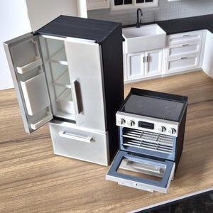 Könnte beinhalten: Ein Miniatur-Puppenhausküchenset bestehend aus einem schwarz-silbernen Kühlschrank mit offener Tür, die Innenfächer zeigt, und einem passenden schwarz-silbernen Herd mit Glaskeramikkochfeld sowie einer offenen Backofentür mit Gitterrost.