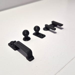 Könnte beinhalten: Vier schwarze Schrankbeschlagteile sind auf einer weißen Oberfläche angeordnet. Die Beschläge umfassen einen Griff, zwei Knöpfe und ein Paar Griffe. Die Teile bestehen aus einem soliden, matten Material.