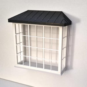 May include: A small white window with a black roof. The window features a grid design and is set against a white backdrop. The roof has a textured finish.