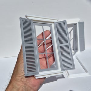 Könnte beinhalten: Ein Miniatur-Fensterrahmen mit weißem Rahmen und grauen Lamellenläden. Das Fenster verfügt über ein sechs-teiliges Gitterdesign. Die Struktur ist mit einem oberen Sturz und einer unteren Fensterbank konstruiert, ein detailliertes Modellbauteil.