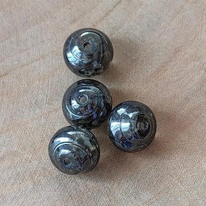 Könnte beinhalten: Vier schwarze und silberne runde Perlen mit einem Wirbelmuster. Die Perlen haben ein Loch in der Mitte.