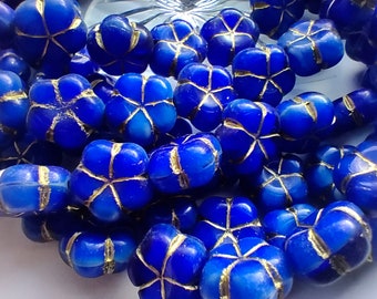 Puede incluir: Una hebra de cuentas de vidrio azul con acentos dorados. Cada cuenta tiene forma de flor con cinco pétalos.