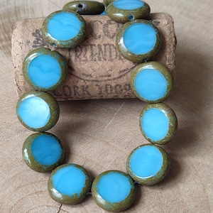 May include: A strand of round, turquoise blue glass beads with a green, mottled glaze. The beads are strung on a wire and are arranged in a circle.