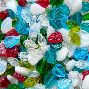 May include: A collection of colorful glass beads in various shapes, including leaves, hearts, and teardrops. The beads are a mix of clear, green, blue, red, and white.