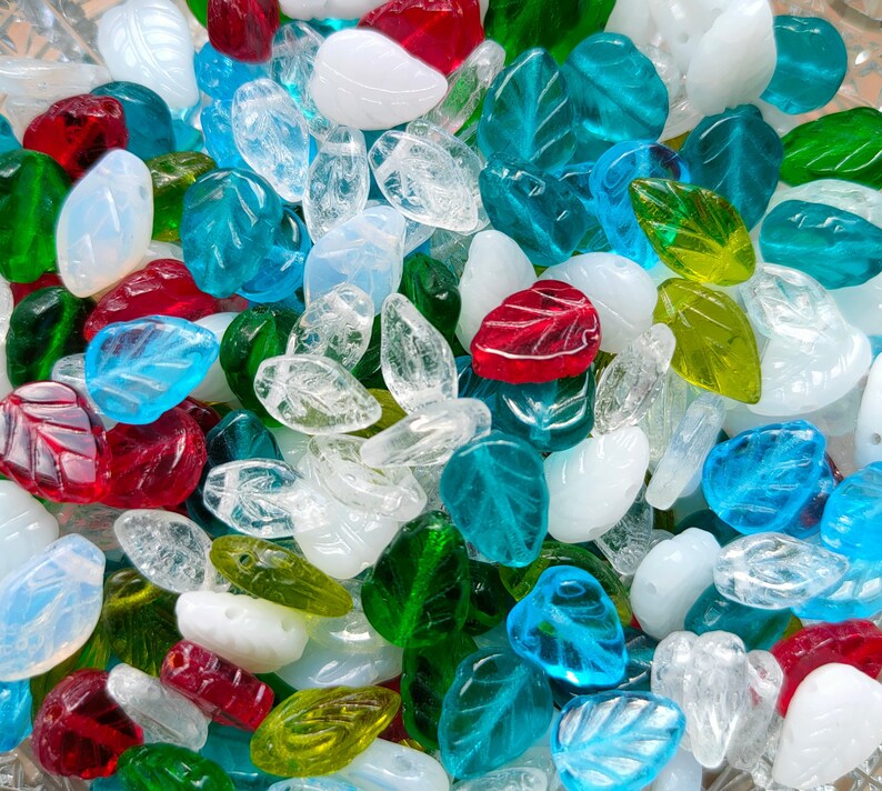 May include: A collection of colorful glass beads in various shapes, including leaves, hearts, and teardrops. The beads are a mix of clear, green, blue, red, and white.