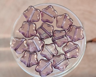 May include: A collection of 14 star-shaped glass beads in a light purple colour with a shimmery finish.