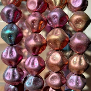 Peut inclure: Un brin de perles de verre irisées dans des tons de rose, d'or et de turquoise. Les perles ont une surface facetée et texturée et sont enfilées sur un fil transparent.