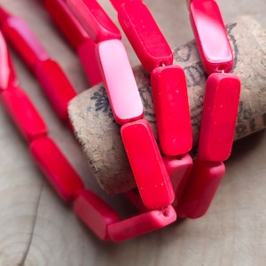 Könnte beinhalten: Eine Reihe von leuchtend roten rechteckigen Perlen aus Kunststoff, die in einem Muster angeordnet sind. Die Perlen sind übereinander gestapelt und liegen auf einer Korkoberfläche.