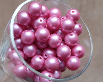 May include: A clear glass filled with numerous pink, spherical beads. Each bead has a lustrous, pearlescent sheen and a small hole. Suitable for jewellery making or various craft activities.