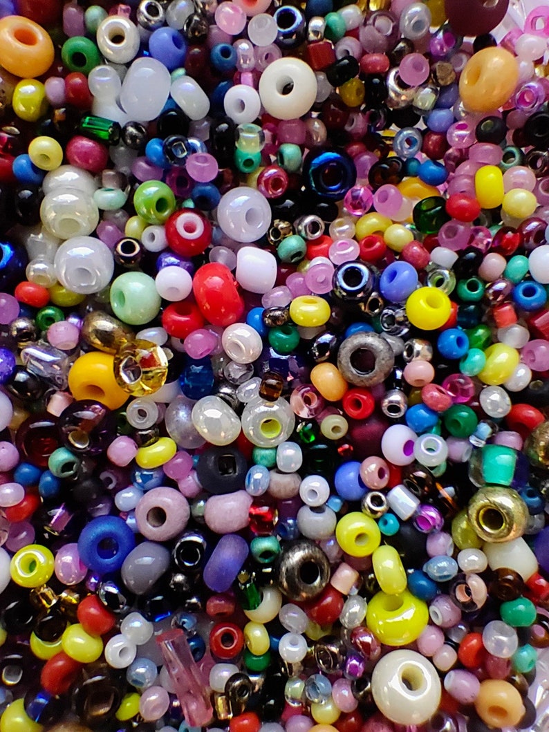 May include: A large assortment of colorful glass beads in various shapes and sizes. The beads are a mix of opaque and transparent colors, including red, blue, green, yellow, and white.