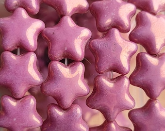 May include: A close-up of a pile of pink star-shaped ceramic beads. The beads have a glossy finish and are arranged in a random pattern.
