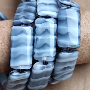 May include: A strand of grey and white glass beads with a wavy pattern. The beads are rectangular and have a glossy finish.