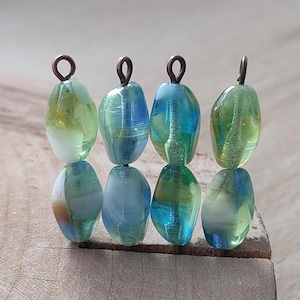 May include: Six glass beads with a mix of green, blue and white colours. Each bead has a copper wire loop at the top for hanging.