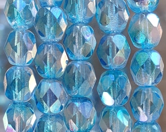 Può includere: Una collana di perline di vetro blu iridescente. Le perline sono sfaccettate e hanno una forma leggermente arrotondata.