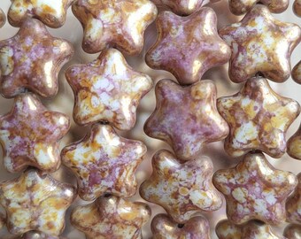 May include: A close-up of a group of ceramic star-shaped beads. The beads are a mix of white, gold, and pink with a marbled effect.